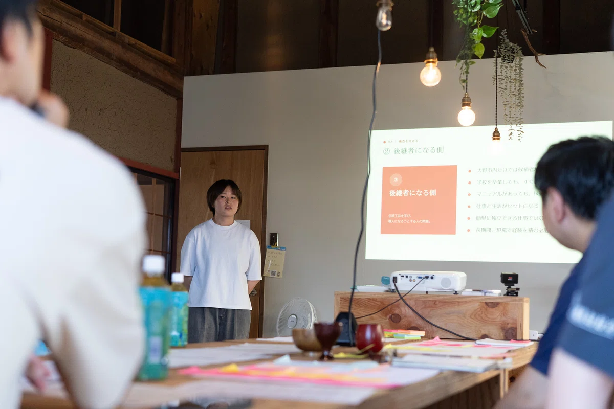 古民家の一室で、参加者が「後継者になる側」と題したスライドを投影しながら発表している様子。テーブルには付箋を貼った模造紙が広げられている